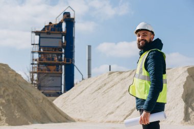İnşaat mühendisi, güneşli bir günde beton üretim tesisinin planlarını tutuyor.