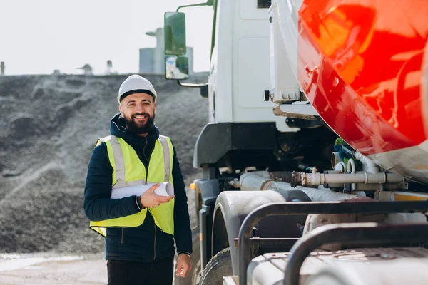 Elinde planlar olan gülümseyen mühendis, çimento kamyonunun yanında güvenle duruyordu.