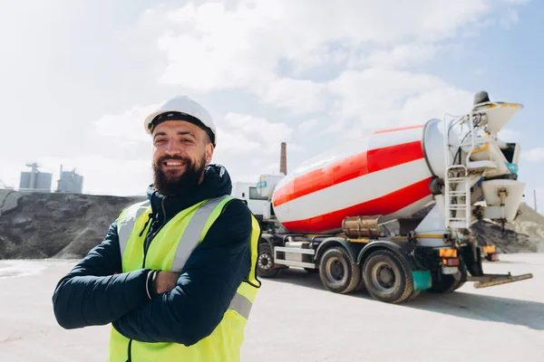 Beton üretim tesisinde kolları çapraz duran gülümseyen bir inşaat işçisinin portresi.