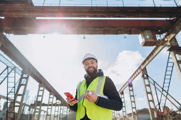 Elinde planlar olan mühendis, beton üretim tesisinde çalışmalara nezaret ederken akıllı telefon kullanıyor ve etkili bir iletişim ve ilerleme sağlıyor.