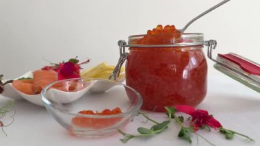 Arka planda büyük kavanozda tuzlu kırmızı somon yumurtası havyarı. Somon havyarlı tuzlu yumurta tatmak. Elin kaşıkla cam kaseden havyar alır. Yavaş çekimde yakın çekim.. 