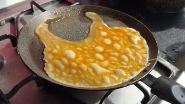 Professional chef wearing black gloves showcasing the delicious process of cooking an omelette. Witness the expert cooking techniques. The video captures the flipping of eggs, the use of a spatula.