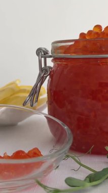 Arka planda büyük kavanozda tuzlu kırmızı somon yumurtası havyarı. Somon havyarlı tuzlu yumurta tatmak. Elin kaşıkla cam kaseden havyar alır. Yavaş çekimde yakın çekim.. 