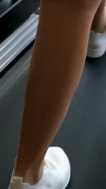 Portrait of young blonde woman runs on modern treadmill near panoramic window side view. Slim athletic lady exercises with trainer machine in luxury gym slow motion. Vertical shot. High quality 4k