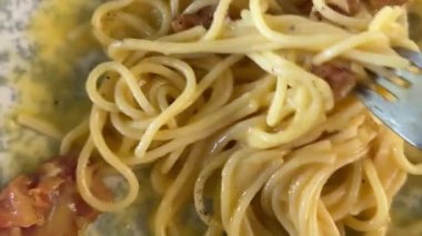 mesmerizing moment captured as a fork gracefully spins through a plate of creamy carbonara. The twirl accentuates the rich textures, creating a visual that invites. stir spaghetti carbonara