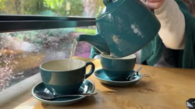 cozy restaurant woman pours tea In emerald green cup autumn Cold Warmth Comfort couples drinking tea wooden table. High quality 4k footage