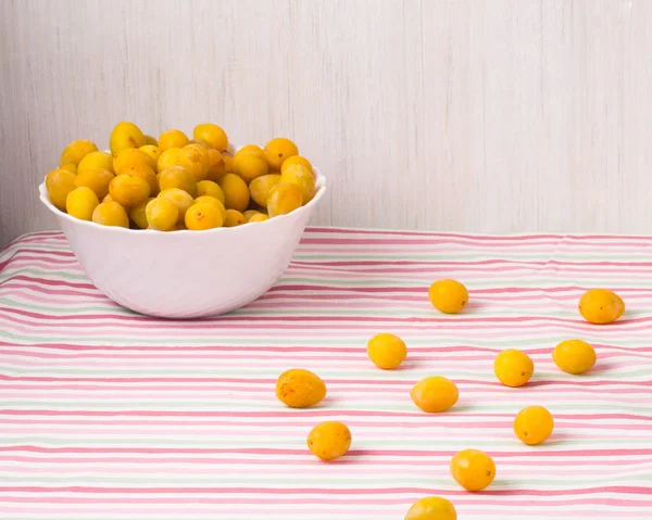 Sarı erikler beyaz kasede renkli çizgili masa örtüsünde. Vege — Stok fotoğraf