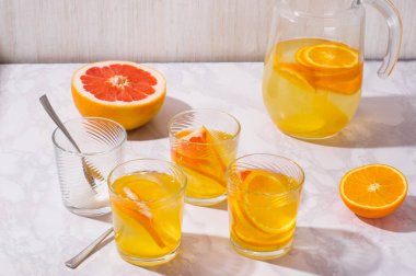 Portakal, limon ve greyfurtlu limonata sürahisi. Beyaz masada bir bardak limonata.
