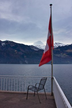 Gölün üzerindeki dağların önünde boş bir sandalye ve bir İsviçre bayrağı: sembolik resim