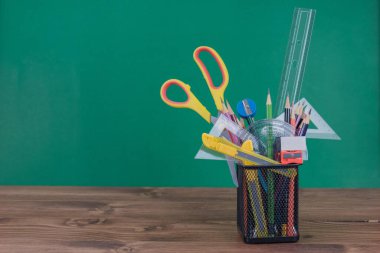 Kutudaki birçok okul malzemesi yeşil arka plandaki ahşabı yerleştirdi..