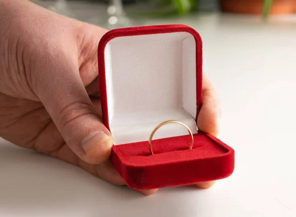 Ehering rote Schachtel umgeben von Rosenblättern. Ein Heiratsangebot. Box mit einem Ring in den Händen eines Mannes auf verschwommenem Hintergrund — Stockfoto