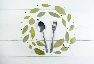 Yiyecek arka planı, defne yaprakları ve çatal bıçak takımları beyaz ahşap arka planda boş alan. Üst görünüm, alanı kopyala.