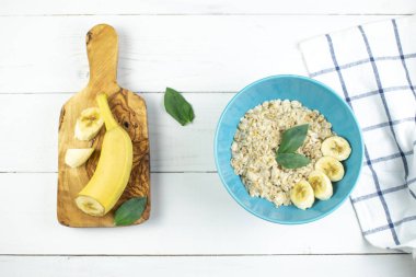 Lezzetli yulaf ezmeli tabak ve beyaz ahşap arka planda muz dilimleri. Kahvaltı imajı, sağlıklı beslenme..