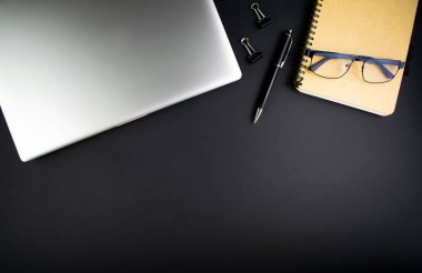 Minimalist iş yeri konsepti, karanlık bir arka planda dizüstü bilgisayar, kalem ve iş kayıtları. Başlangıç olarak iş planının resmi. Üst Manzara. Düzleştirme biçimi.
