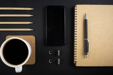 Minimalist iş yeri konsepti, akıllı telefon, kalem ve iş kayıtlarıyla karanlık bir geçmişe sahip. Başlangıç olarak iş planının resmi. Üst Manzara. Düzleştirme biçimi.