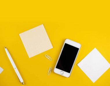 Minimalist iş yeri konsepti, akıllı telefon, kalem ve iş kayıtları ile sarı arka planda. Görüntü dijital ajansı, online eğitim. Üst Manzara. Düzleştirme biçimi.