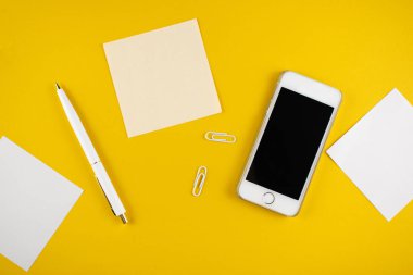 Minimalist iş yeri konsepti, akıllı telefon, kalem ve iş kayıtları ile sarı arka planda. Görüntü dijital ajansı, online eğitim. Üst Manzara. Düzleştirme biçimi.