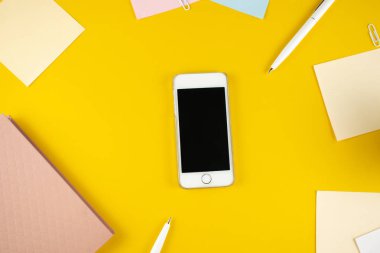 Minimalist iş yeri konsepti, akıllı telefon, kalem ve iş kayıtları ile sarı arka planda. Görüntü dijital ajansı, online eğitim. Üst Manzara. Düzleştirme biçimi.