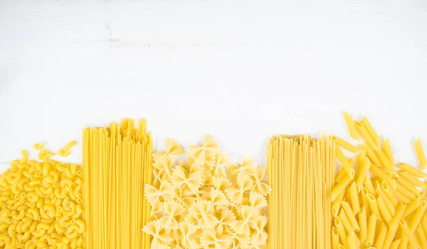 Vários tipos de massas em uma mesa de madeira branca. Conceito de cozinha italiana, ingredientes alimentares. Deitado. Vista superior, espaço de cópia — Fotografia de Stock