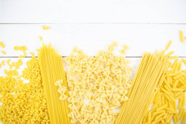 Beyaz ahşap bir masada çeşitli makarna türleri. İtalyan mutfağı konsepti, yemek malzemeleri. Düz yatıyordu. Üst görünüm, alanı kopyala