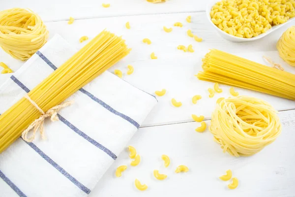 various types of pasta on a white wooden table. Italian cuisine concept, food ingredients. Close up view