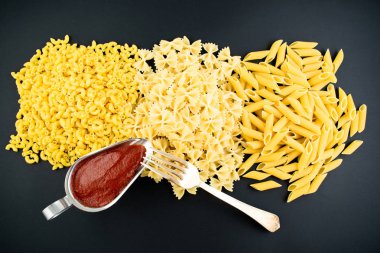 Koyu arkaplanda çeşitli makarna çeşitleri var. İtalyan mutfağı konsepti, yemek malzemeleri. Düz yatıyordu. Üst görünüm, alanı kopyala