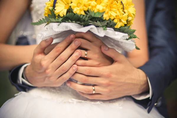 Hands of the bride and groom close-up. They have wedding rings on their fingers. The bride is holding a beautiful yellow bouquet of yellow. Wedding day.