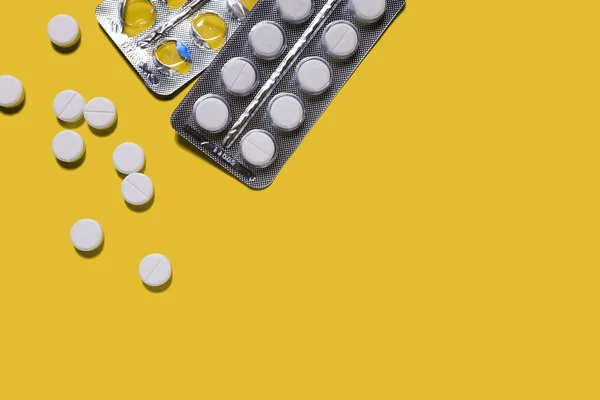 Pack of tablets. White pills on a yellow background. Antibiotics or aspirin in Packed and scattered on the surface. Copy space for text.