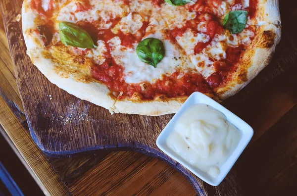 Slices of vegetarian pizza with mozzarella cheese, tomatoes, spices and fresh Basil. Delicious Italian pizza. Sliced pizza Margarita on a wooden Board.