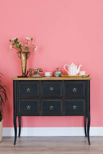 Old chest of drawers isolated on pink wall background . Next is a flower in a pot. Beautiful interior in vintage style.
