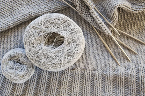 Incomplete knitting project with metal knitting needles close-up. Gray threads, skeins and tangles of Italian wool yarn. The concept of knitting, needlework, handmade.