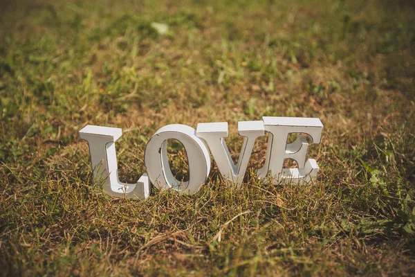 The word love in English of white wooden letters on the green grass in the Park outdoors, copy space. Decoration for wedding, Valentine\'s Day, engagement. Concept of love