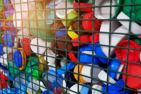 Multi-colored plastic screw caps from bottles behind an iron grid. Concept: waste management, environmental protection, separate waste collection. Plastic waste.