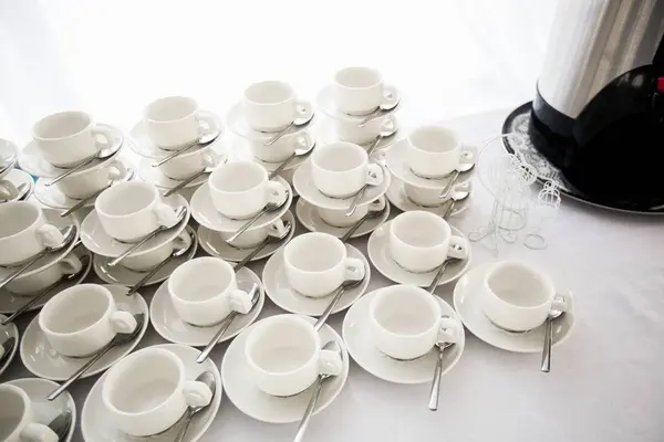 A range of traditional clean empty ceramic coffee cups on the table in the restaurant. Lots of white cups on saucers for serving tea or coffee for Breakfast, at the buffet event.