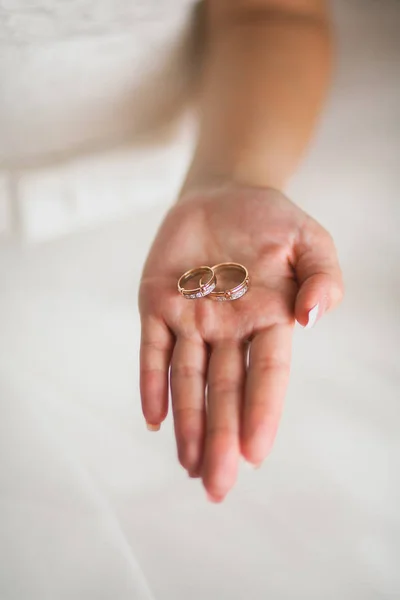 Wedding engagement rings on the bride\'s palm, blurred background. The bride in a white dress holds beautiful expensive gold rings of the newlyweds, decorated with precious stones.