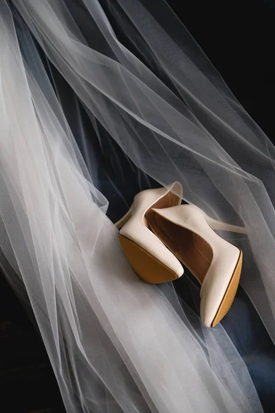 Designer wedding beige bride shoes on an expensive velour sofa, tulle or veil. Women\'s new modern fashion high-heeled shoes, genuine leather. Morning preparations for the wedding.