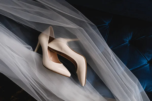Designer wedding beige bride shoes on an expensive velour sofa, tulle or veil. Women\'s new modern fashion high-heeled shoes, genuine leather. Morning preparations for the wedding.