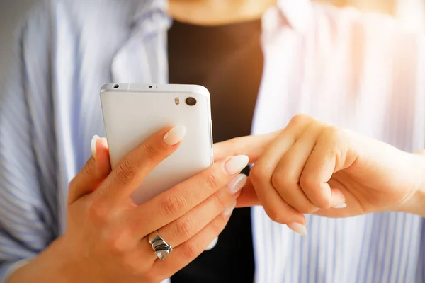 Mobile phone in the hands of a stylish fashion girl freelancer. A young woman in a black t-shirt and striped shirt, with a beautiful manicure holding the phone. Blurred background
