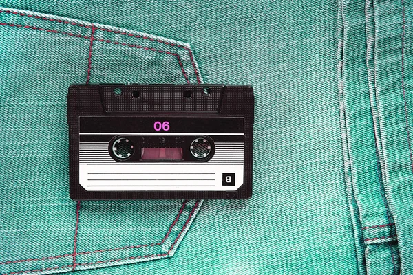 Vintage retro audio cassette on the background of green jeans, close-up. Media technologies of the past 80-ies. Conceptual picture to illustrate the memories of the past. The view from the top.