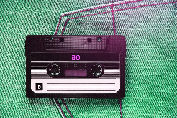 Vintage retro audio cassette on the background of green jeans, close-up. Media technologies of the past 80-ies. Conceptual picture to illustrate the memories of the past. The view from the top.