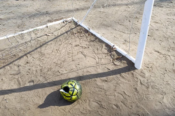 A torn deflated ball on the sand, near the football goal on a Sunny summer day, forgotten or thrown on the football field. Sports background with copy space for text.