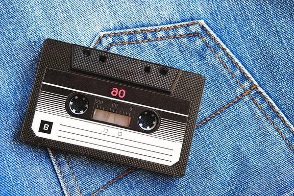 Vintage retro audio cassette on the background of blue jeans, close-up. Media technologies of the past 80-ies. Conceptual picture to illustrate the memories of the past. The view from the top.