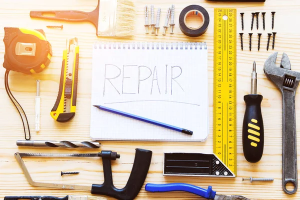Notebook with the word repair, a mug of tea and tools for building a house or apartment repair, on a wooden table. The workplace of the foreman. The theme of home and professional repair, construction