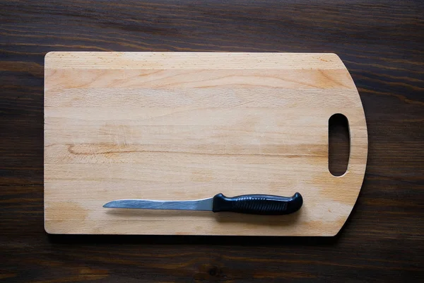 Kitchen knife with black plastic handle on a wooden cutting Board, close-up. Copy space for text. The concept of kitchen utensils, cooking.