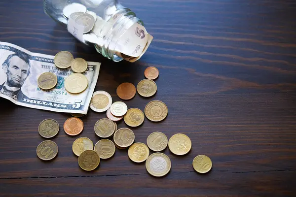 Banknotes, dollars, and coins of different countries on the background of a wooden table. Next to the glass jar with the inscription in English Home, symbolizes the piggy Bank. Business concept.