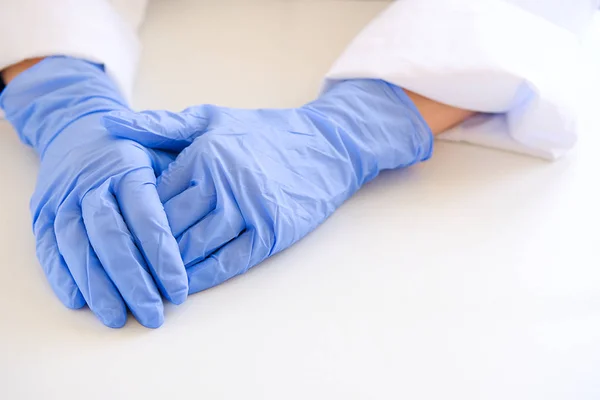 Hands of the attending physician in medical rubber gloves on the background of a white table, close-up. Doctor in scrubs with a stethoscope. The concept of health, pharmacy and medicine.