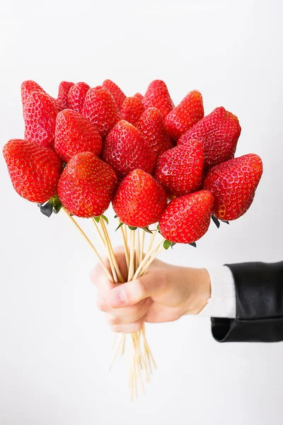 Alternative edible bouquet of berries in the hand of a man or woman, birthday, Valentine\'s Day, holiday, close-up. Whole strawberry fruit on wooden skewers, on a white background. Selective focus.