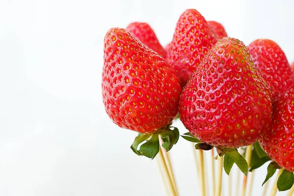 Collection of whole strawberry fruit on wooden skewers isolated on white background. Alternative edible bouquet of berries for birthday, Valentine\'s Day, holiday, close-up. Selective focus.