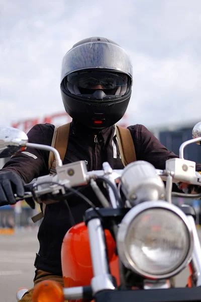 Biker man or guy-racer in a protective helmet and glasses sitting on a motorcycle classic style, looking at the camera in the Parking lot at the shopping center. The concept of active sports lifestyle