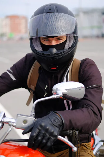 Biker man or a boy-racer in the helmet sitting on the motorcycle in classic style, looking at camera, on the free Parking at the shopping center or store. The concept of active sports lifestyle.